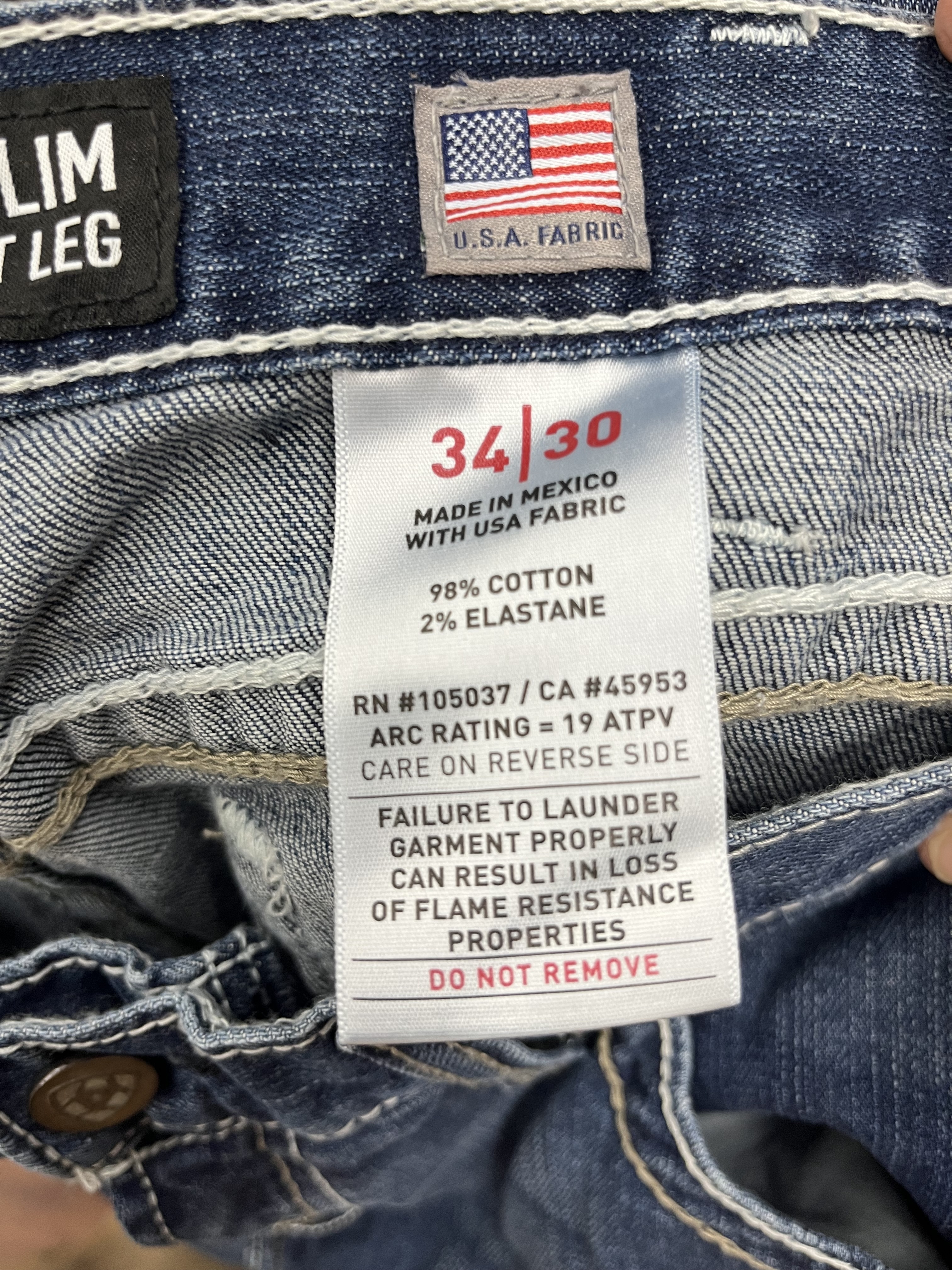 Ariat flame-resistant jeans label showing 19 ATPV arc rating, 98% cotton and 2% elastane fabric content, and warning about improper laundering.