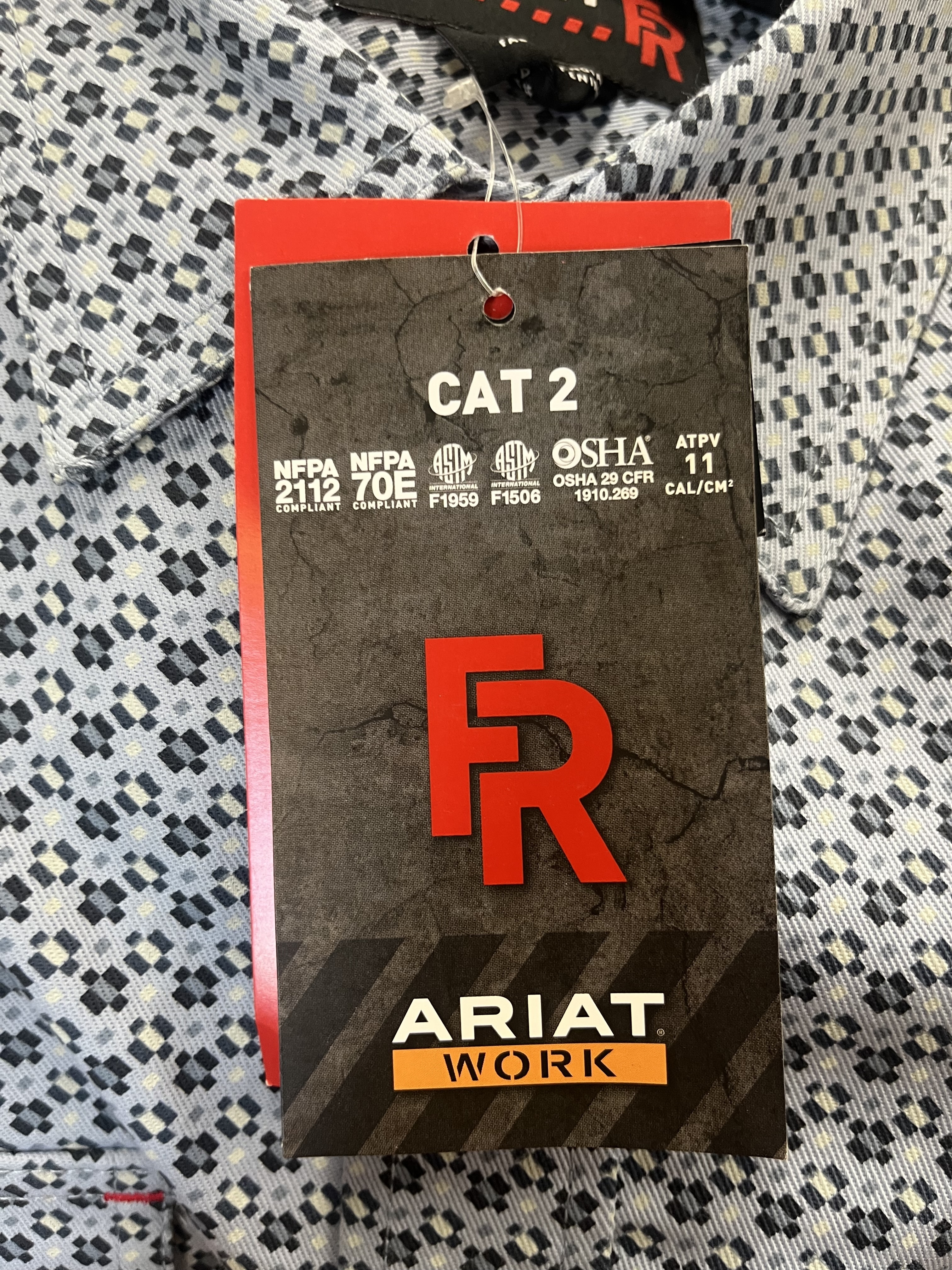 Ariat FR shirt hangtag showing CAT 2, ATPV 11 cal/cm&sup2;, and applicable safety standards.